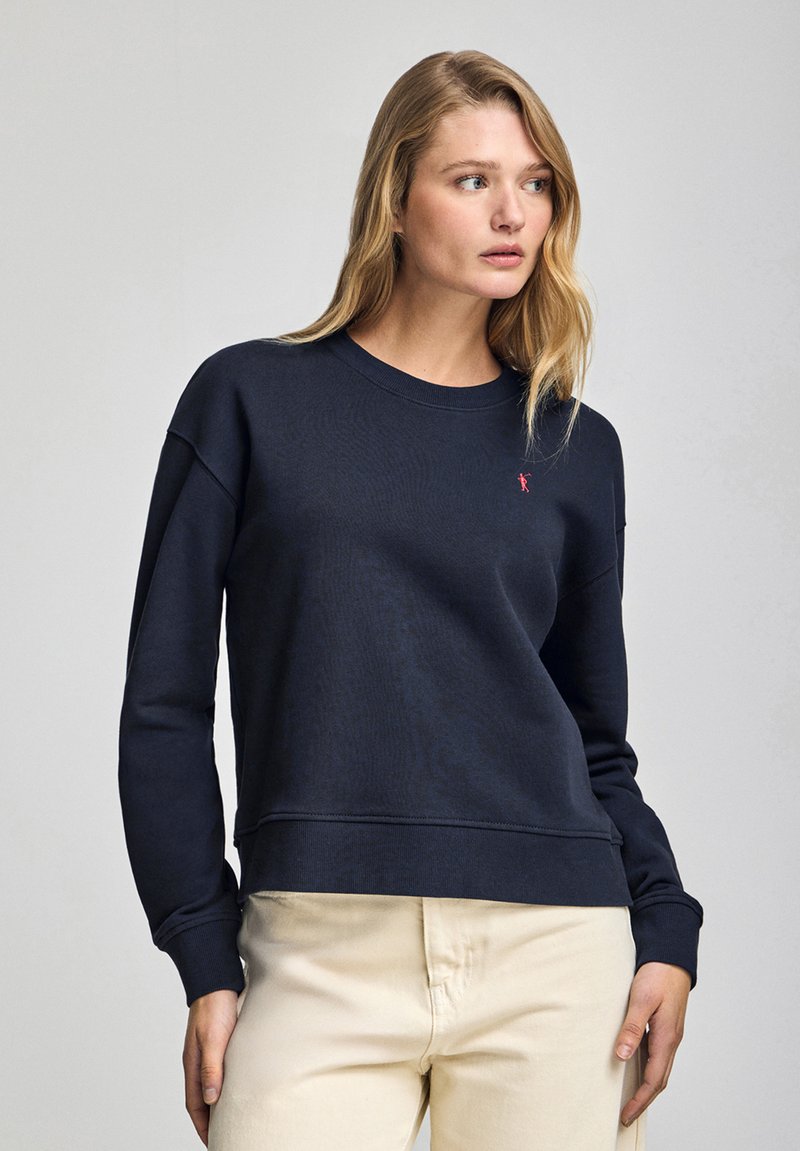 Mörkblå bomulls sweatshirt med rund hals, ribbade ärmslut och en liten röd logotyp på bröstet. Avslappnad stil med en bekväm passform.