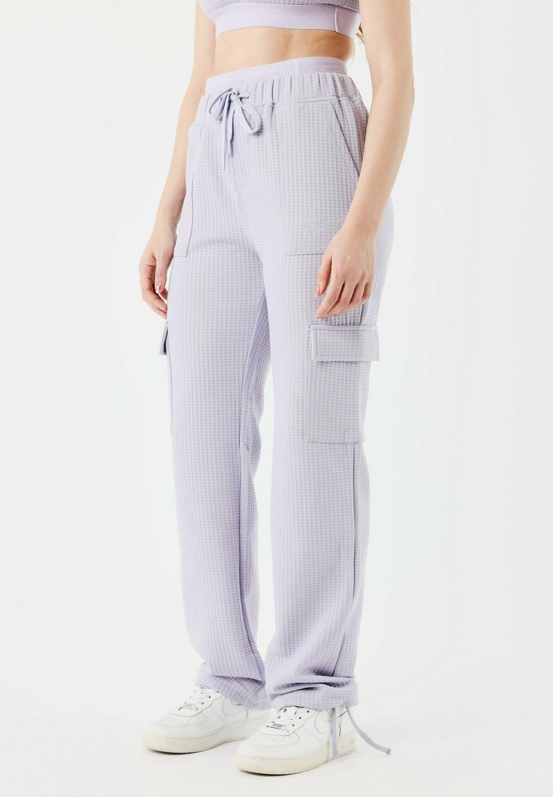 Pantalons cargo lavande clair avec un motif en tricot gaufré texturé, taille élastique et plusieurs poches, associés à des baskets blanches.