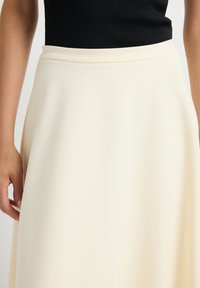 Crème A-lijnrok van zacht materiaal, met een gladde textuur en een passende tailleband. Het ontwerp reikt tot de vloer met een vloeiende val.