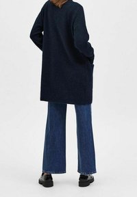 Navy long sweater made of soft fabric, paired with wide-leg blue jeans. Shoes are black, chunky, with a smooth texture and minimal detailing.