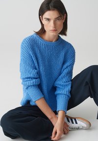 Maglione azzurro lavorato a maglia con scollo rotondo e polsini a coste, abbinato a pantaloni scuri e sneakers. Tessuto testurizzato con vestibilità ampia.