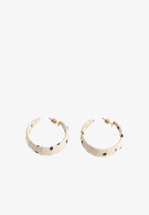 Ohrringe mit creméfarbenem Stoff bezogenem Bügel, schwarzen unregelmäßigen Punkten und goldfarbenen Metallsteckern und -verschlüssen.