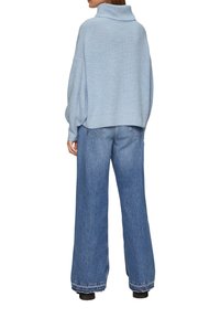 Hellblaues, übergroßes Sweatshirt mit hohem Kragen, kombiniert mit weiten Jeans. Das Sweatshirt hat ein strukturiertes Strickmuster und gerippte Bündchen.