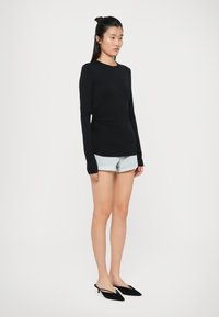 Top nero a maniche lunghe con design aderente, tessuto morbido e aperture per il pollice, abbinato a pantaloni shorts in denim e scarpe nere a punta.
