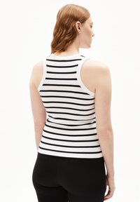 Canotta a righe bianche e nere con una texture a coste, che presenta un design aderente e spalline larghe, abbinata a pantaloni neri.