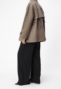 Chaqueta marrón de gran tamaño con detalle de solapa, cierres con botones y un ajuste relajado, combinada con pantalones negros anchos con rayas verticales.