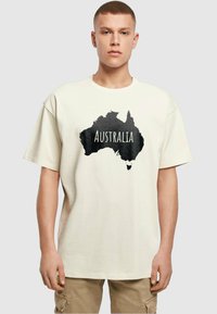 Kremo spalvos marškinėliai su juodu Australijos siluetu ir žodžiu "AUSTRALIJA", atspausdintu ryškiai baltai. Laisvas kirpimas.