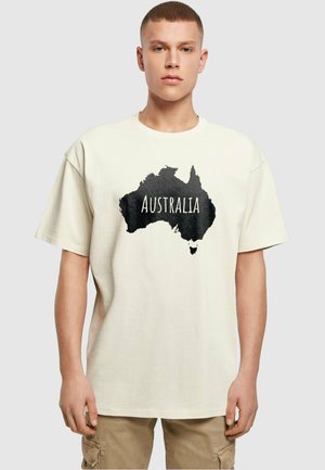 Cremefarvet t-shirt med en sort silhuet af Australien, hvor ordet "AUSTRALIEN" er trykt fremtrædende i hvid. Løs pasform.