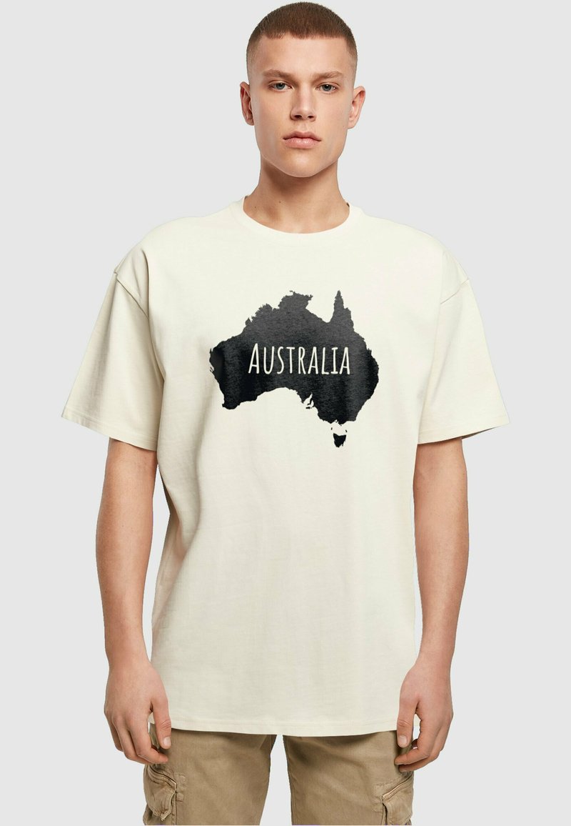 Kremo spalvos marškinėliai su juodu Australijos siluetu ir žodžiu "AUSTRALIJA", atspausdintu ryškiai baltai. Laisvas kirpimas.