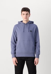 Felpa in cotone viola con tasca a marsupio frontale, cappuccio regolabile con coulisse e patch con logo sul petto. Presenta polsini e orlo a coste.