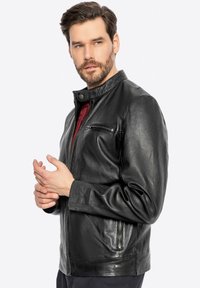 Giacca da uomo in pelle nera con colletto alto, tasca sul petto con zip e tasche laterali. Texture liscia, design aderente, dettagli di cucitura discreti.