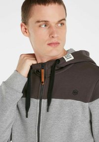 Gray and dark gray zip-up hoodie with a textured finish, adjustable drawstring hood, and logo detail on upper chest.