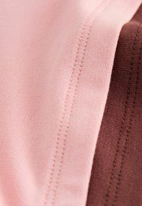 Gros plan sur un tissu rose et marron avec des coutures parallèles et une texture douce.