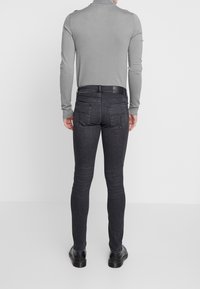 Sittande mörkgrå jeans med en strömlinjeformad design, med en solid textur, bakfickor och en svart bältesdetalj. Bärs med en ljusgrå topp.