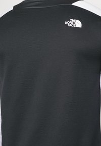 Maglietta sportiva nera con texture e accenti bianchi, caratterizzata da un piccolo logo nella parte superiore della schiena e un design a girocollo.