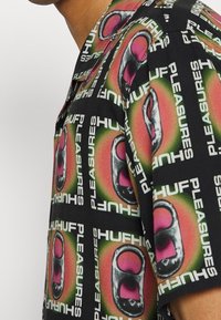 Camicetta senza colletto a maniche corte con una vivace stampa grafica multicolore che presenta accenti neri, rosa e verdi su uno sfondo nero.