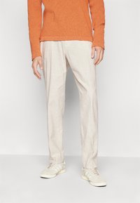 Beige linnedbukser med en afslappet pasform, parret med en struktureret orange sweater og lys grå sneakers med hvide striber.