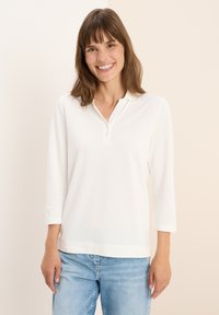 Witte polo met driekwartmouwen en een kraag, met een knoopsluiting en een licht afgeronde zoom. Zachte, lichte stof.