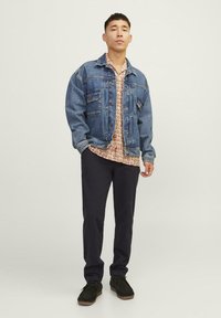 Denim jaka ar izbalinātu zilo krāsu, divas krūšu kabatas; ziedu raksta krekls zem tā; tumšas bikses; melnas kurpes ar brūnu zoli.