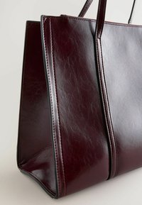 Burgunderfarbene faux Leder Tote Bag mit strukturierter Form, doppelten Griffen und kontrastierenden Nähten, ausgestattet mit einer glatten, glänzenden Textur.