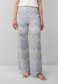 Pantalons à jambes larges avec un motif en zigzag dans des teintes de violet clair, vert et blanc ; fabriqués à partir d'un tissu léger et texturé.