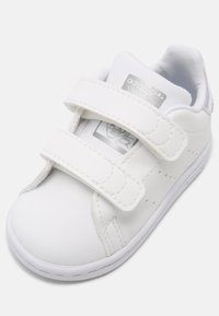 Sneaker bianco in pelle con cinturini in velcro, punta arrotondata, dettagli perforati e un sottile marchio sulla linguetta e sul tallone.