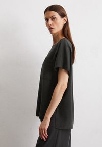Dunkelgrünes kurzärmliges T-Shirt mit lässiger Passform, Fronttasche und rundem Ausschnitt. Weicher Stoff mit glatter Textur.