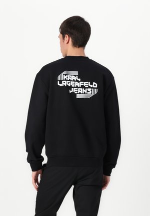 Black sweatshirt featuring a large white graphic text on the back that reads "KAAI LAGERFELD JEANS," with ribbed cuffs and hem.