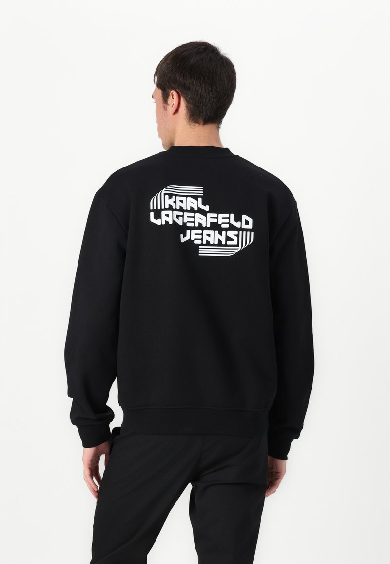 Sweatshirt preto com um grande texto gráfico branco nas costas que diz "KAAI LAGERFELD JEANS", com punhos e bainha canelados.