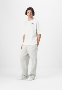 Hvit kortermet t-skjorte med et fargerikt grafisk trykk. Kombinert med lysegrå, løstsittende joggebukser og hvite sneakers.