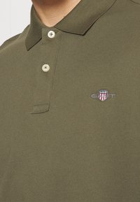 Olijfgroen polo-shirt met een kraag, voorzien van drie knopen en een klein geborduurd logo op de linkerborst. Gestructureerde stof.