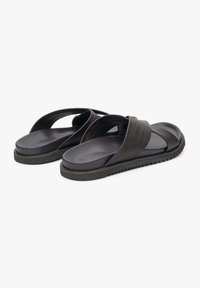 Czarne, płaskie klapki z krzyżowym paskiem, wykonane z teksturowanego materiału syntetycznego, z grubą, żłobioną podeszwą dla lepszej przyczepności.