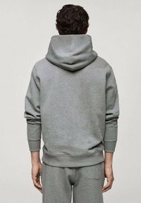 Felpa grigia realizzata in tessuto morbido, caratterizzata da un grande cappuccio, polsini e orlo a coste, e vestibilità rilassata. Design semplice senza loghi o motivi visibili.