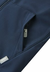 Marineblaue Stoff mit einer Reißverschlusstasche und einem kleinen Markenetikett, das ein schlankes und funktionales Design betont.