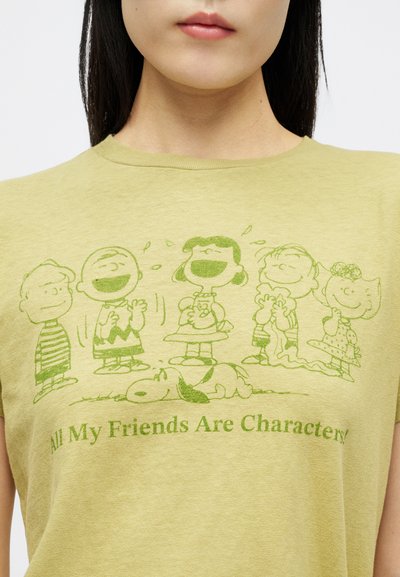 Άτομο που φοράει ένα ανοιχτό πράσινο μπλουζάκι με πράσινους χαρακτήρες Peanuts που γελούν και κοιμούνται, το κείμενο λέει "Όλοι οι φίλοι μου είναι χαρακτήρες!"
