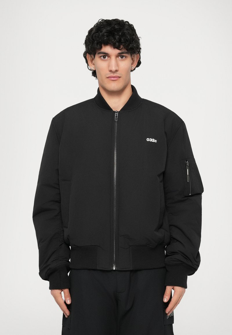 Giacca bomber nera con chiusura a zip, colletto a coste e polsini. Dotata di tasche laterali e tasca sulla manica sinistra. Tessuto liscio e imbottito.