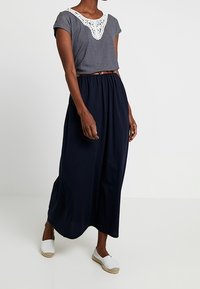 Striped gray short-sleeve top with lace detail at neckline, paired with a flowy navy maxi skirt and white espadrille shoes.