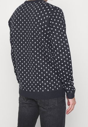Le pull en maille bleu marine présente un motif de losanges blancs répétitif, des poignets et un ourlet côtelés, ainsi qu'un col ras du cou classique.