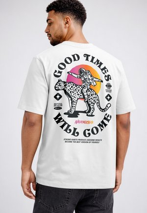 Man wearing white T-shirt with an astronaut riding a spotted leopard under a sunset and phrase "Good Times Will Come".