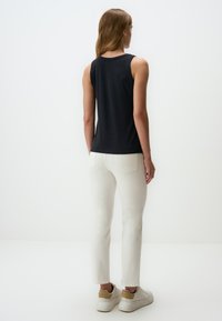 Top senza maniche nero abbinato a jeans bianchi aderenti e sneakers di colore chiaro. Tessuto liscio con un design semplice. Sfondo pulito e neutro.