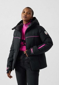 Giacca imbottita nera con cappuccio, caratterizzata da accenti rosa e patch con logo. Superficie testurizzata, doppie tasche frontali e polsini aderenti.