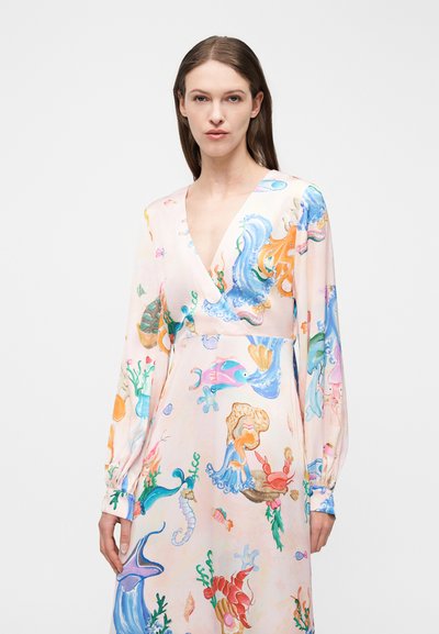 Γυναίκα που φοράει φόρεμα με μακριά μανίκια και σχέδια με θέμα το υποβρύχιο περιβάλλον, όπως ψάρια, χταπόδι, καβούρι και φύκια, σε ένα απλό φωτεινό φόντο.