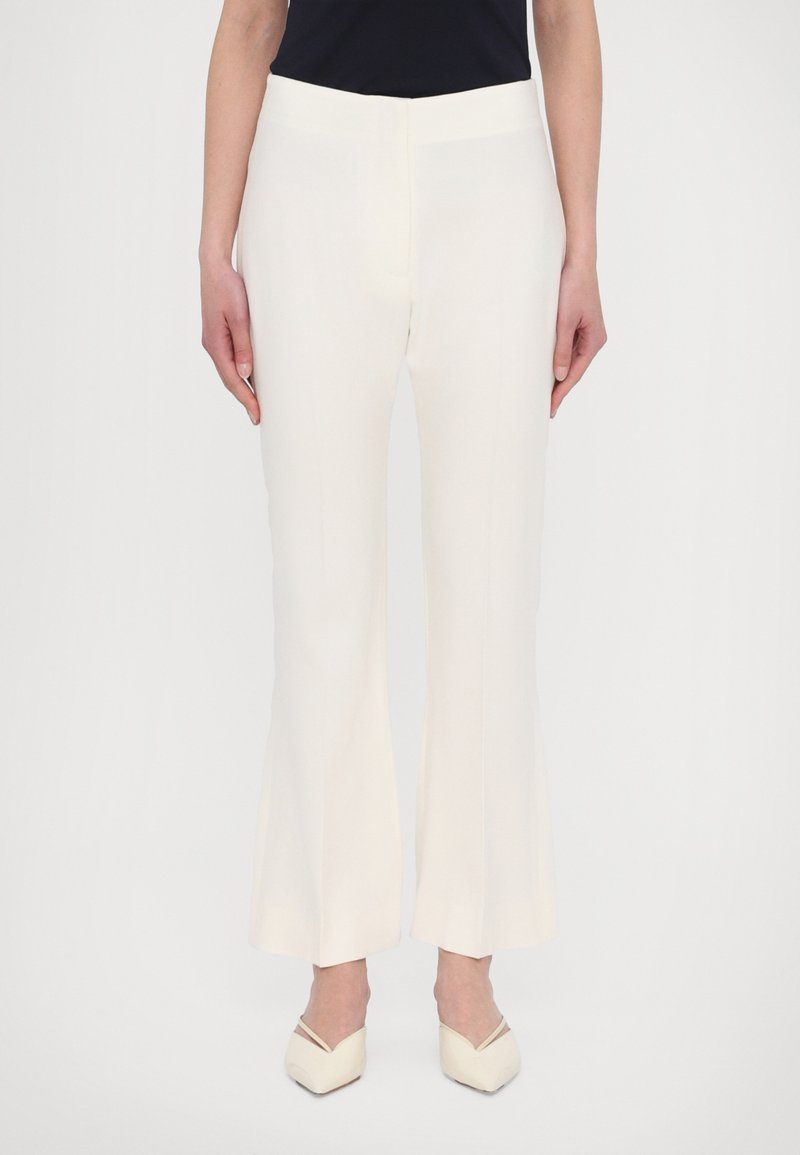 Witte, uitlopende broeken gemaakt van gladde stof, met een aansluitende taille en subtiele verticale naden. Gecombineerd met beige, pumps met een spitse neus.