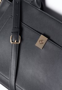 Svart fusk läderhandväska med gyllene detaljer, i rektangulär form, justerbar rem och ett dekorativt spänne med blomsterdesign.