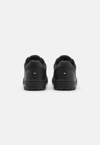 Sorte lædersneakers med struktureret finish, der har en polstret krave, robust sål og et lille logo-patch i rød, hvid og blå.