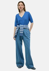 Pull en V bleu tricoté à manches courtes, associé à un pantalon taille haute bleu clair à jambes larges, avec un détail de ceinture rayée à nouer.