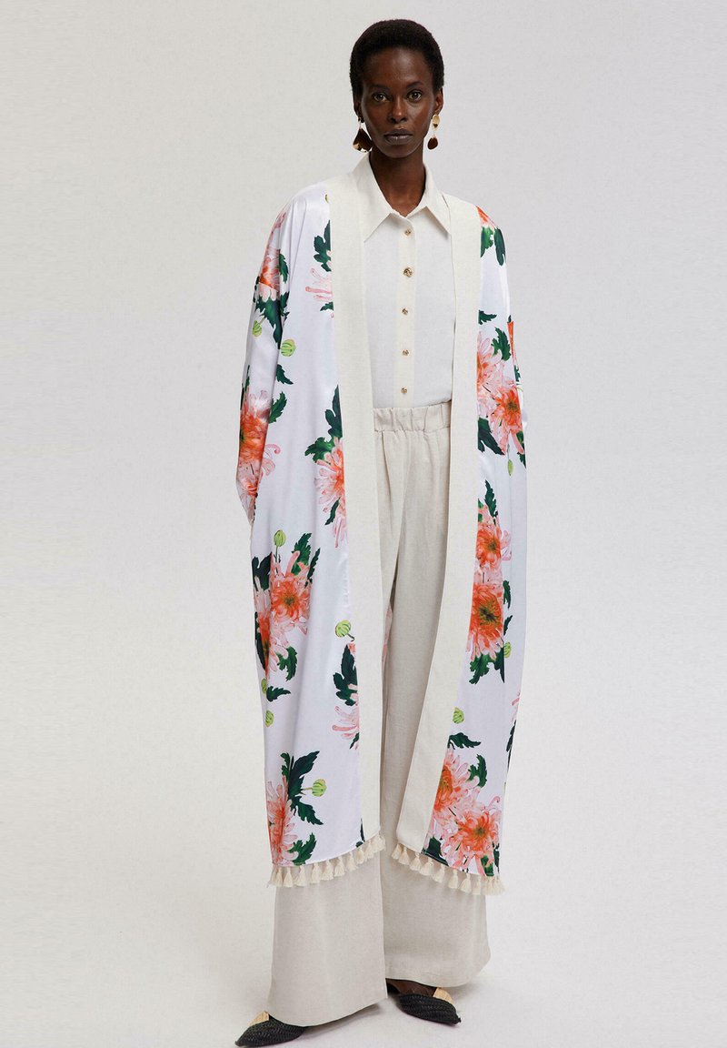 Kvetinový kimono s ružovými a zelenými kvetmi na bielom pozadí, s krémovým lemovaním a tkanicami. Skombinované s košeľou na gombíky a béžovými nohavicami.