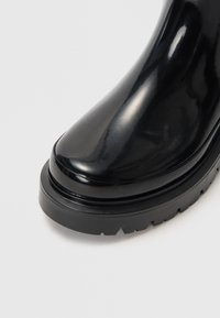 Stivale alla caviglia lucido nero con punta arrotondata, suola in gomma platform con battistrada e texture liscia. Nessuna cucitura o dettaglio hardware visibile.