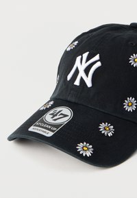 Μαύρο ρυθμιζόμενο καπέλο baseball με λευκό κεντητό λογότυπο New York Yankees και λευκά σχέδια μαργαρίτας στο εμπρόσθιο και πλευρικά μέρη.
