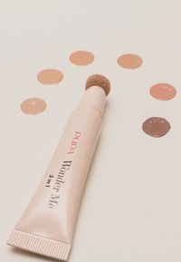 Pupa Wonder Me, ein 3-in-1-Kosmetikschlauch, verfügt über eine weiche, runde Applikatorspitze, umgeben von beigen und braunen Produktmustern.